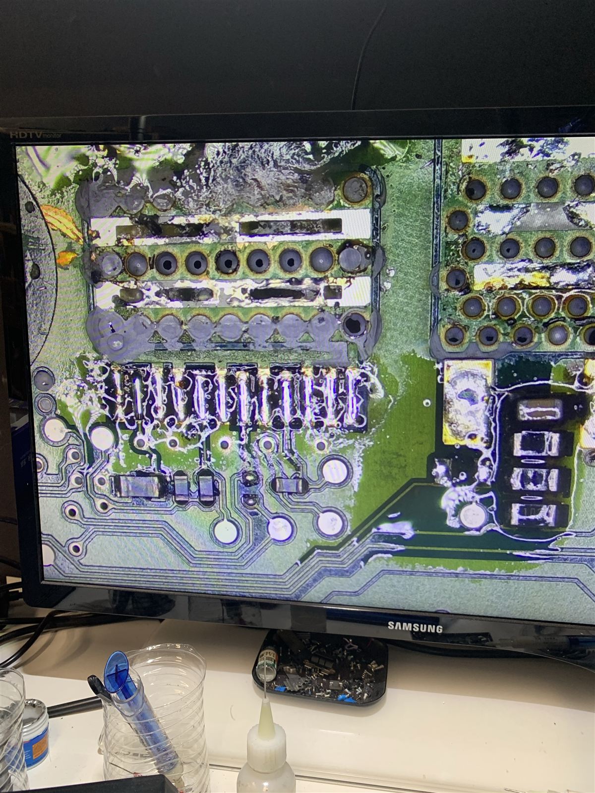 Microscope view on the bench monitor of the ECU circuit board with the VN5012AK removed, showing its row of pads and the heat pad with vias