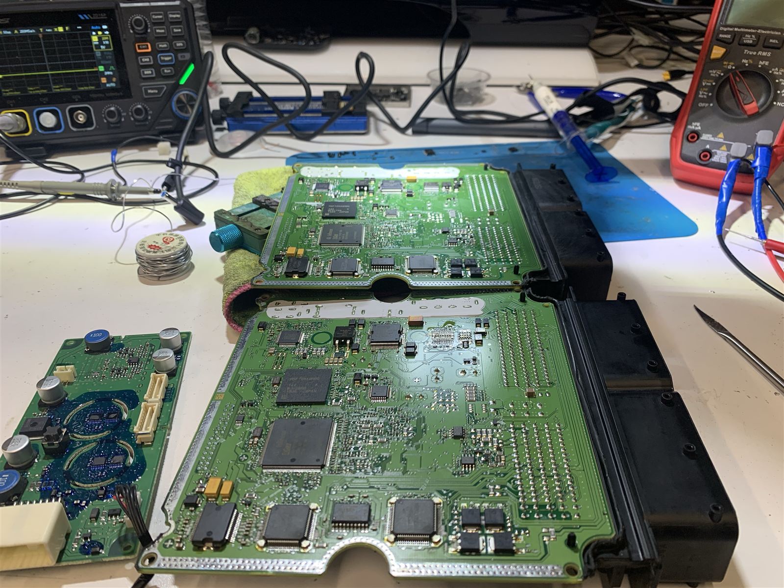 Two Bosch MEDG17.9.8 ECU boards side by side on the CQ Electronics bench with an oscilloscope and multimeter